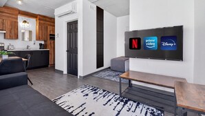 A modern living space with a flat-screen TV displaying streaming services, a kitchen area, and a seating area with a rug. - Loft 306 | Rooftop | Downtown (Rimouski)