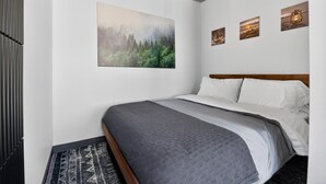 A bedroom with a bed, a painting, and three smaller artworks on the wall. - Loft 306 | Rooftop | Downtown (Rimouski)