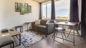 Un salon moderne comprenant un canapé, une table basse, une table à manger avec des chaises et une grande fenêtre avec des rideaux.