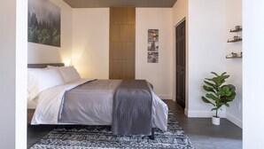 Une chambre à coucher moderne avec un lit, une lampe fixée au mur, une plante et un tableau.