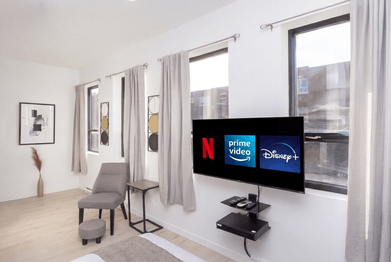 Un salon moderne doté d’un téléviseur à écran plat diffusant des services de streaming, d’un fauteuil gris, d’un petit pouf et d’une décoration minimaliste.