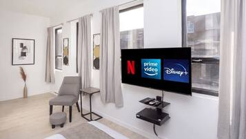 Un salon moderne doté d’un téléviseur à écran plat diffusant des services de streaming, d’un fauteuil gris, d’un petit pouf et d’une décoration minimaliste.