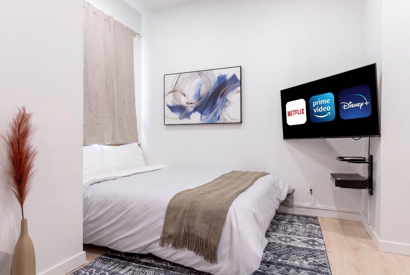 Een slaapkamer met een bed, een televisie waarop streamingdiensten worden getoond, een wandplank en een decoratief schilderij.