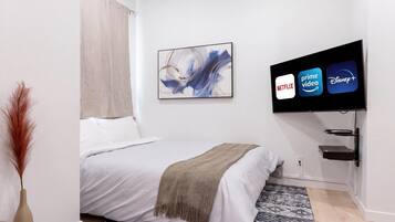 Een slaapkamer met een bed, een televisie waarop streamingdiensten worden getoond, een wandplank en een decoratief schilderij.