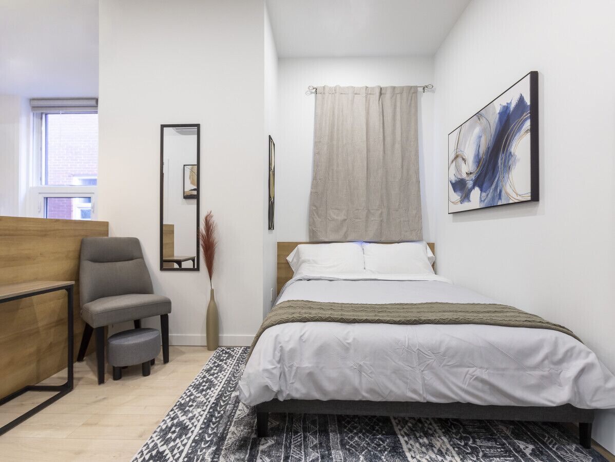 Une chambre moderne avec un lit, une chaise, un bureau et une grande fenêtre.