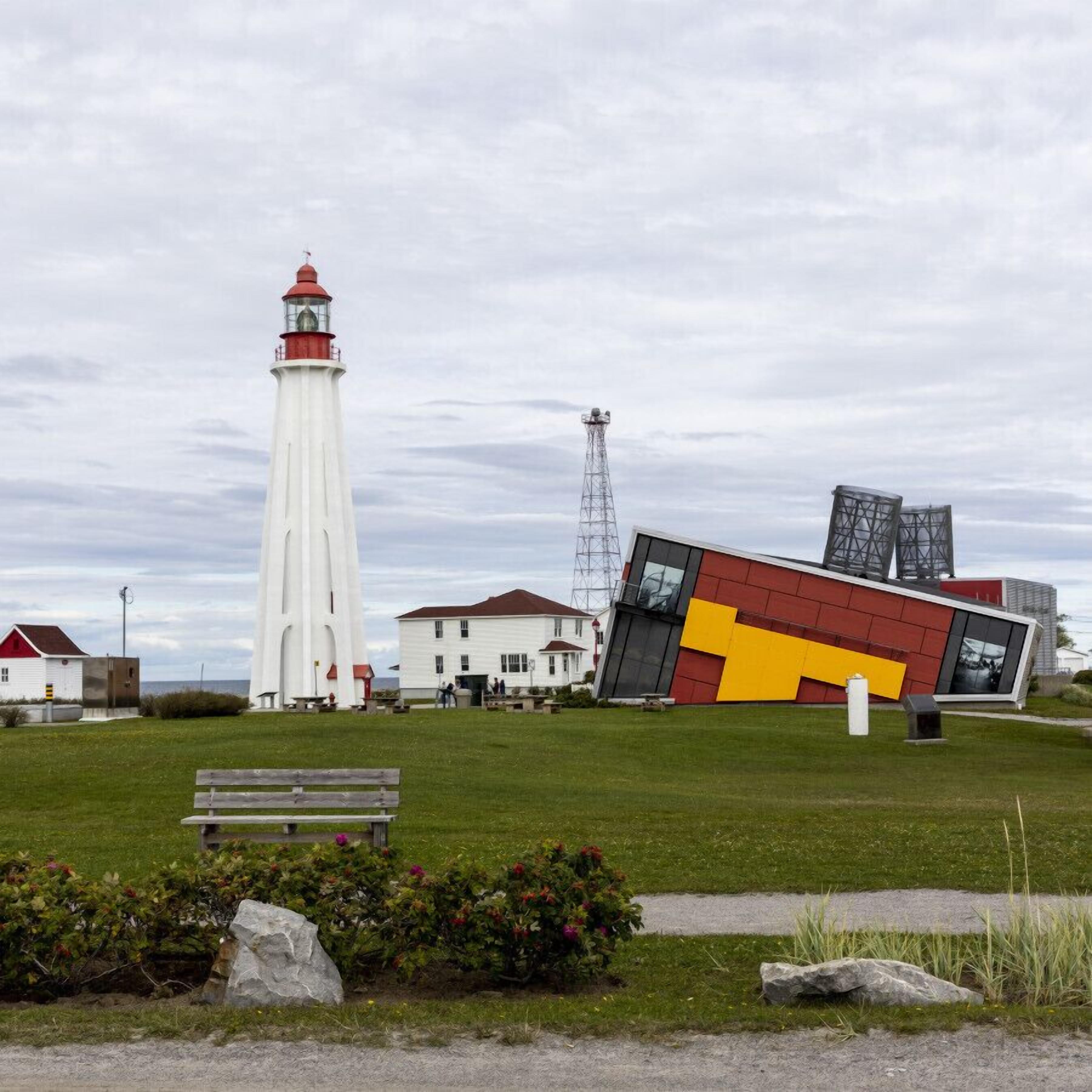 Un phare, un bâtiment moderne et un banc dans un espace verdoyant.