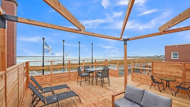 A wooden deck with a table and chairs, a sofa, and a view of the beach and ocean.