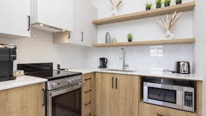 A modern kitchen with a stove, oven, microwave, and a coffee maker. There are wooden cabinets and a white countertop.