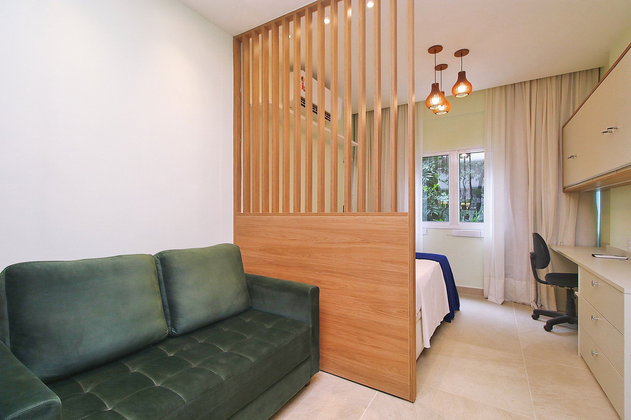 A room with a green sofa, a wooden partition, a desk with a chair, and a window with curtains.