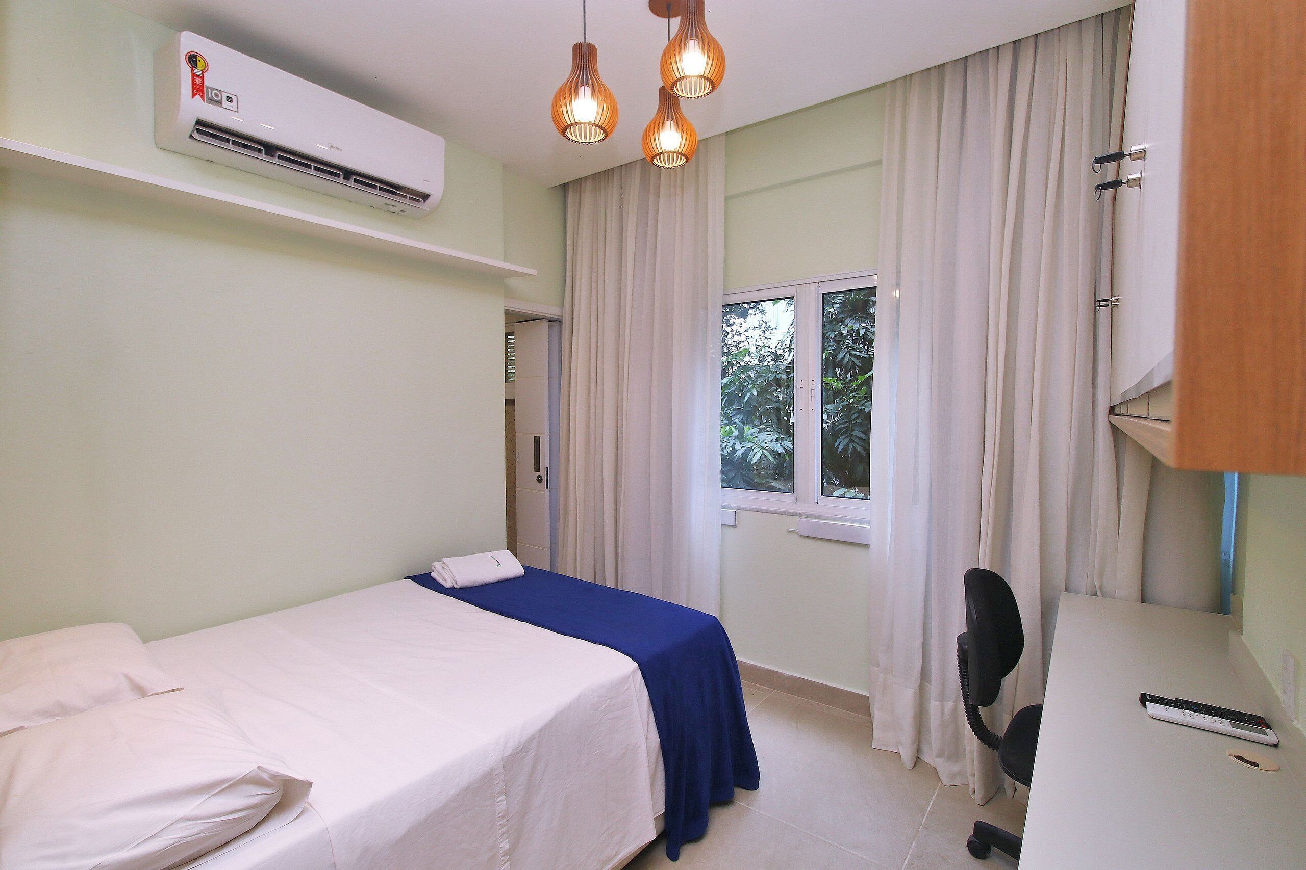A room with a bed, a desk, an air conditioner, and a window with curtains.