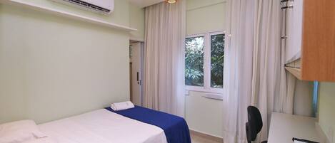 A room with a bed, a desk, an air conditioner, and a window with curtains.