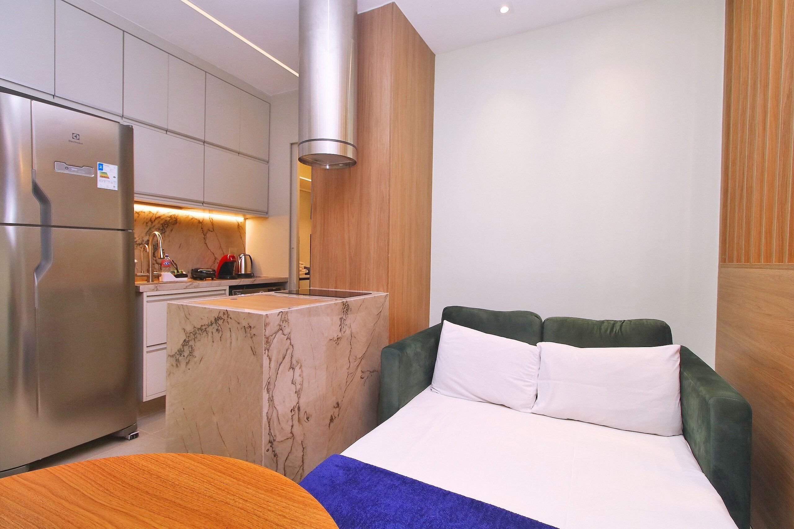 A modern hotel room with a bed, a small kitchen area, and a marble island.