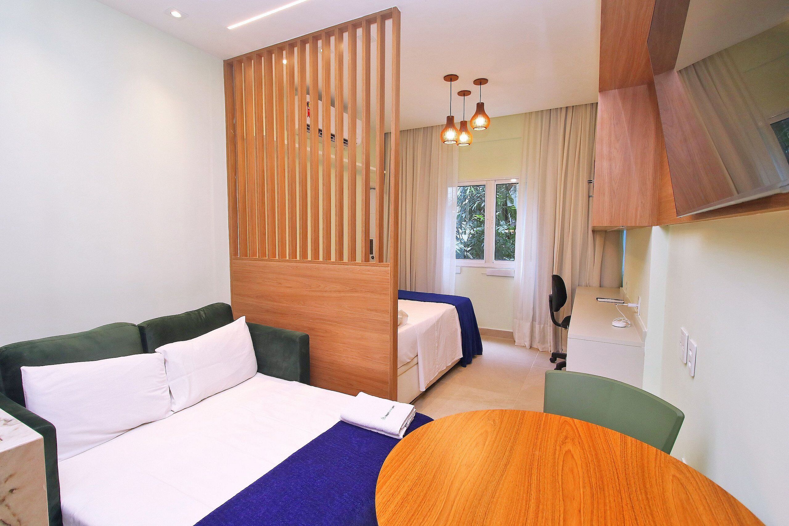 Ein Hotelzimmer mit Bett, Schreibtisch, Stuhl, einer Holzwand und einem Fenster mit Vorhängen.