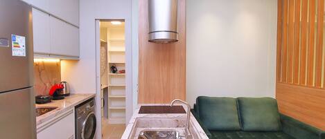 A compact kitchen with a built-in washing machine, a sink, and a green sofa in the adjacent living area.