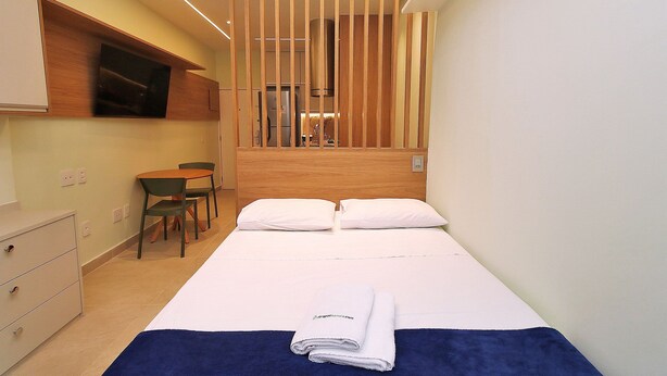 A hotel room with a bed, a desk, a chair, and a TV mounted on the wall. - C061 (Rio de Janeiro)