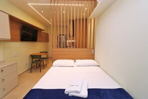 Une chambre d’hôtel équipée d’un lit, d’un bureau, d’une chaise et d’un téléviseur fixé au mur.