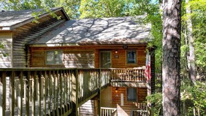 A rustic cabin with a wooden deck and a staircase leading to a second level.