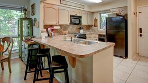 A kitchen with a central island, bar stools, a microwave, stove, refrigerator, and a sign above the microwave.