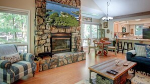 A cozy living room with a stone fireplace, wooden flooring, and a view of the outdoors.