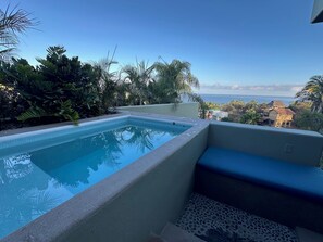 Piscina rectangular con borde de azulejos, rodeada de follaje y con vistas a la costa.