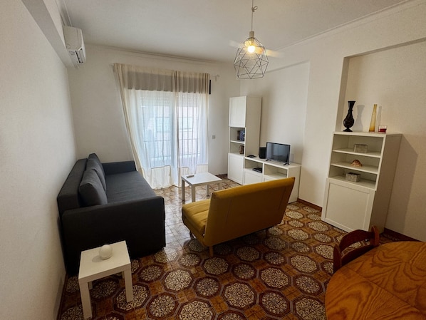 A compact living space with a sofa, a small table, a yellow chair, a TV, and a bookshelf.