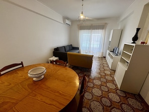 A dining area with a wooden table and chairs, a sofa, a television, and a patterned floor.