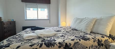 A bedroom with a bed, a dresser, a window with blinds, and a bedside lamp.
