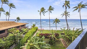 A beachfront property with a view of the ocean, palm trees, and a building with a tiled roof.