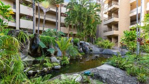 A hotel courtyard with a small pond, lush greenery, and a multi-story building with balconies.