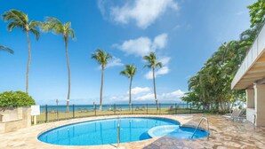 A swimming pool with a stone deck, palm trees, and a view of the ocean.