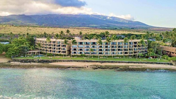 A resort with multiple-story buildings, a beachfront, and a mountainous backdrop.