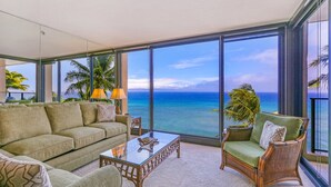 A spacious living room with a large window overlooking the ocean, furnished with a sofa, armchair, and coffee table. - Kaanapali Ocean Front 1 Bedroom! Mahana 617! (Lahaina)