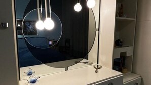 Et badeværelsesbord med et stort spejl, to hængende lys og en hylde med toiletartikler.