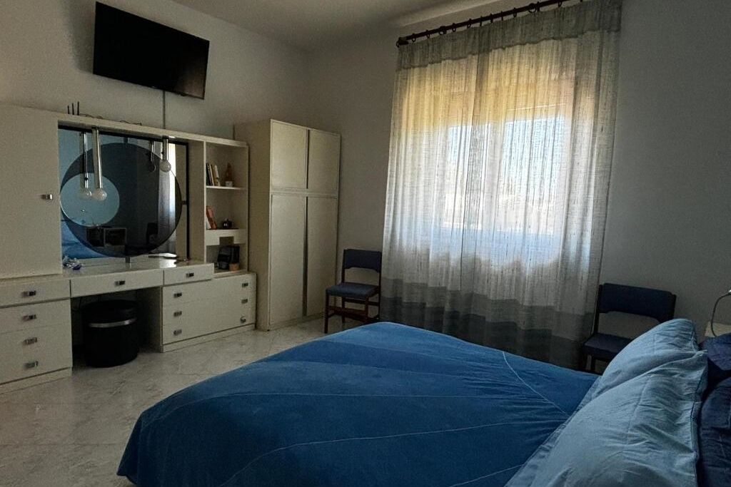 Ein Schlafzimmer mit Bett, Kleiderschrank, Schreibtisch, Stuhl und Fernseher an der Wand.
