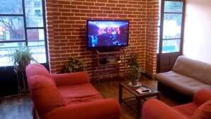 Uma sala de estar com parede de tijolos, uma televisão, dois sofás vermelhos, uma mesa pequena e um vaso com planta.