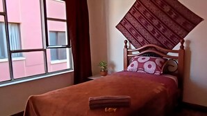 Quarto com cama, janela, mesa de cabeceira e planta em vaso.