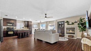 Un salon moderne avec une cheminée, un canapé et un coin cuisine doté d’un plancher en bois foncé.