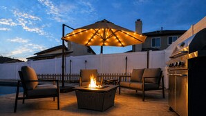 Une terrasse extérieure avec un foyer, des chaises, une table et un barbecue.