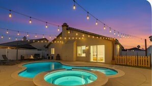 Un jardin avec une piscine et un jacuzzi, des guirlandes lumineuses, et une maison dotée d’une porte-fenêtre coulissante.