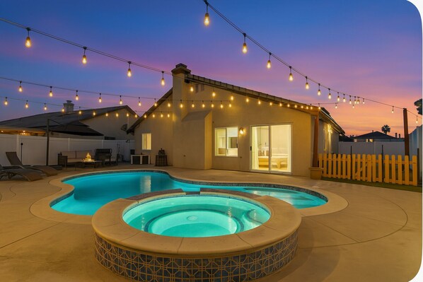A backyard with a swimming pool and hot tub, string lights, and a house with a sliding glass door. - Hemet Haven, Pool, Hot Tub, Backyard, Arcades, Game Room, BBQ Grill and Fire Pit (Hemet)