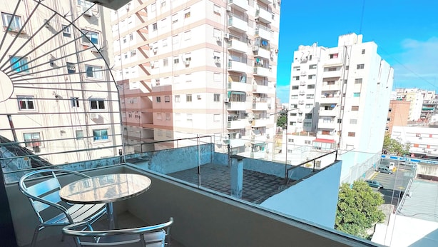 Ein Balkon mit Glastisch und Stühlen, der auf einen Wohnbereich mit mehrstöckigen Gebäuden blickt.