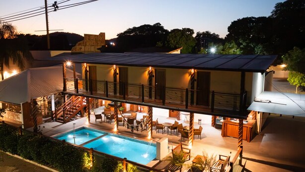 A modern two-story building with a swimming pool, outdoor seating, and a covered patio area. - Pousada Recanto Dourado (Bonito)