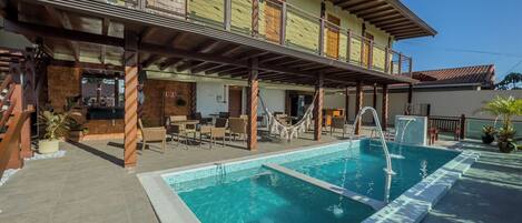 A pool area with a covered seating area, a staircase, and a building with a balcony.