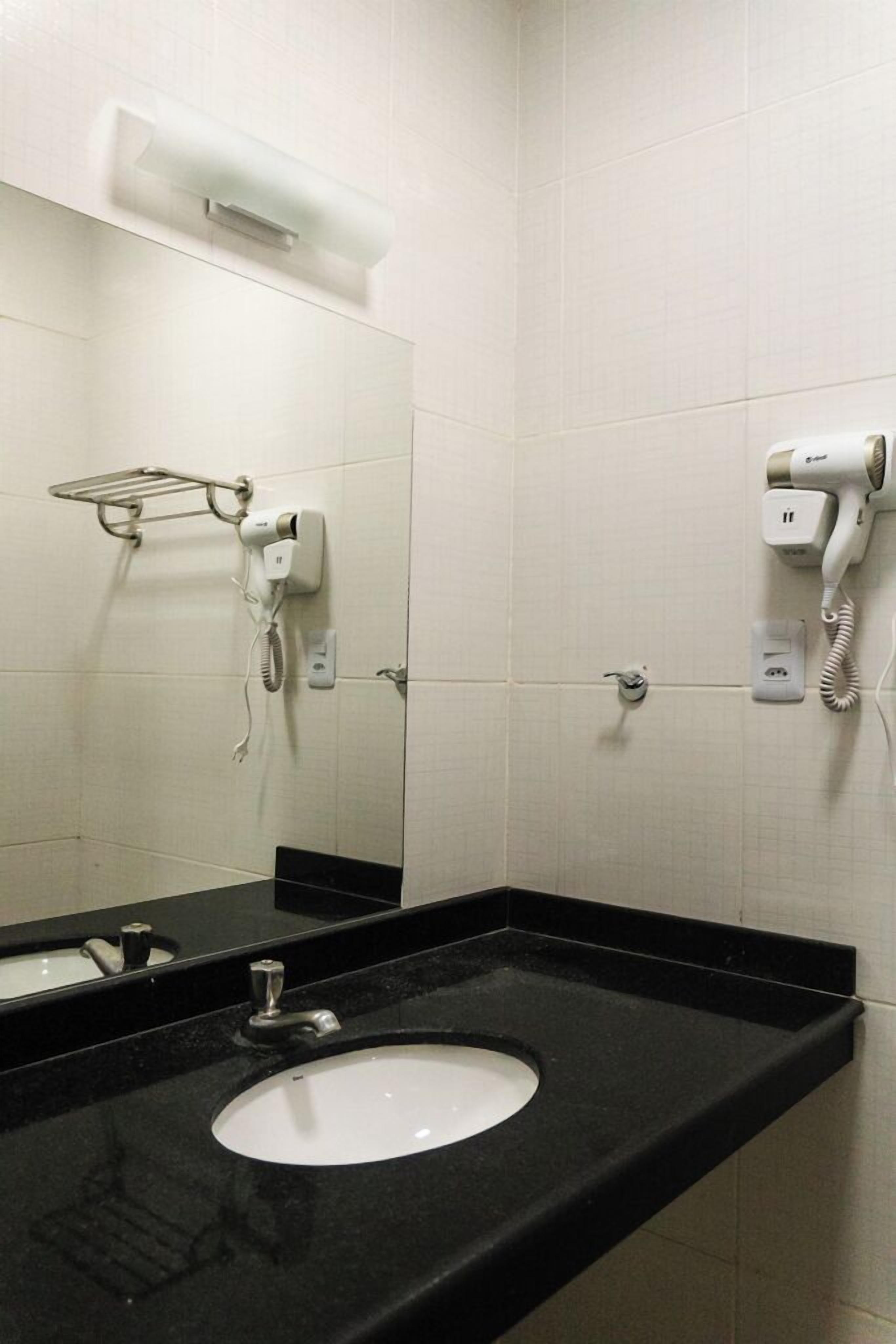 A bathroom with a black countertop, a white sink, a mirror, a hairdryer, and a towel rack.