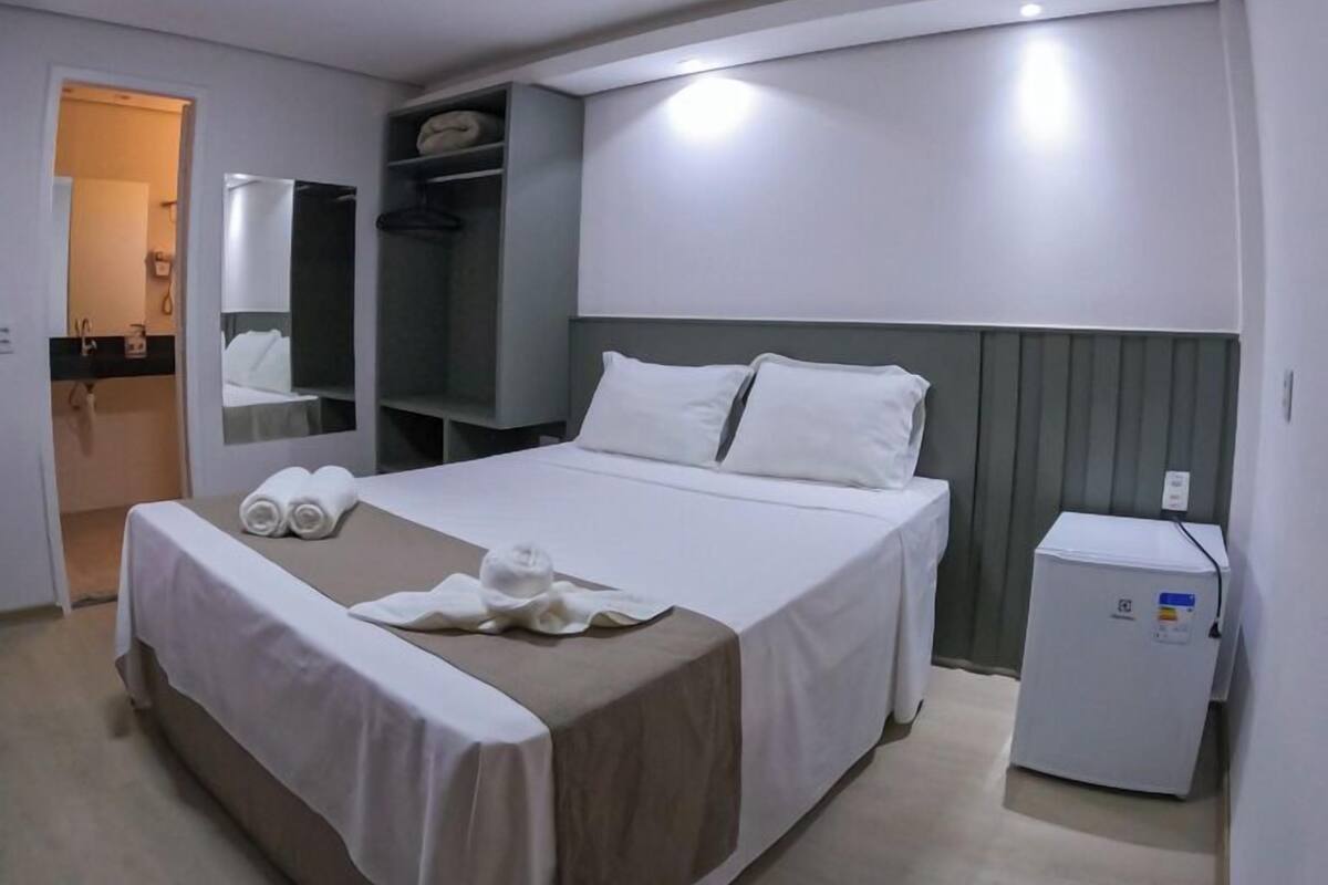 A hotel room with a bed, a small refrigerator, a mirror, and a wardrobe.