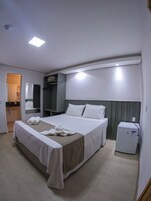 Una habitación de hotel con cama, un refrigerador pequeño, un espejo y un armario.