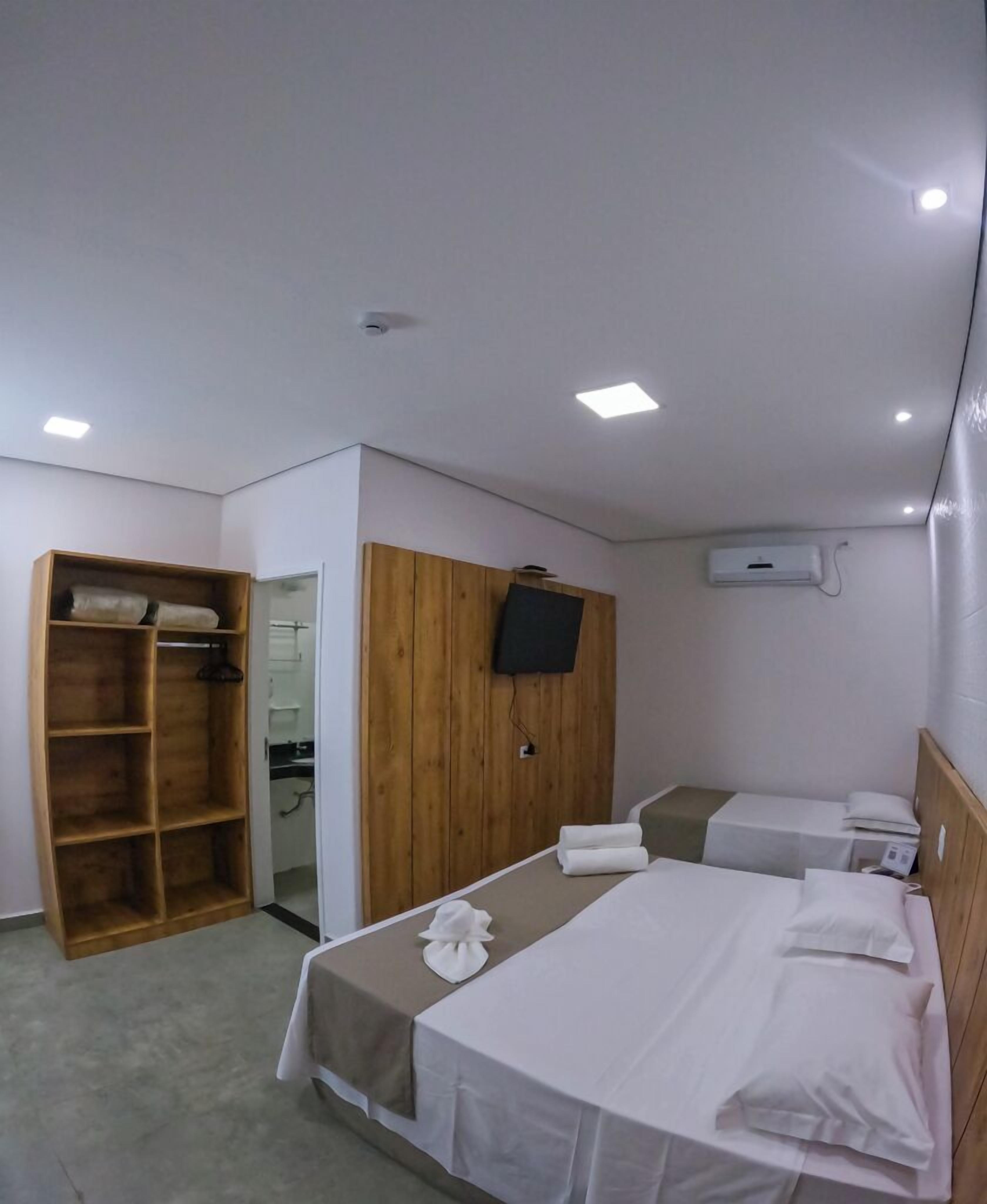 Ein Hotelzimmer mit einem Holzkleiderschrank, einem an der Wand befestigten Fernseher und zwei Betten mit weißer Bettwäsche.