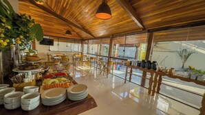 A spacious dining area with a wooden ceiling and large windows, featuring a buffet setup with various dishes and a fruit display. - Pousada Recanto Dourado (Bonito)