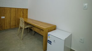 A small, sparsely furnished room with a wooden table, a chair, and a white refrigerator. - Pousada Recanto Dourado (Bonito)