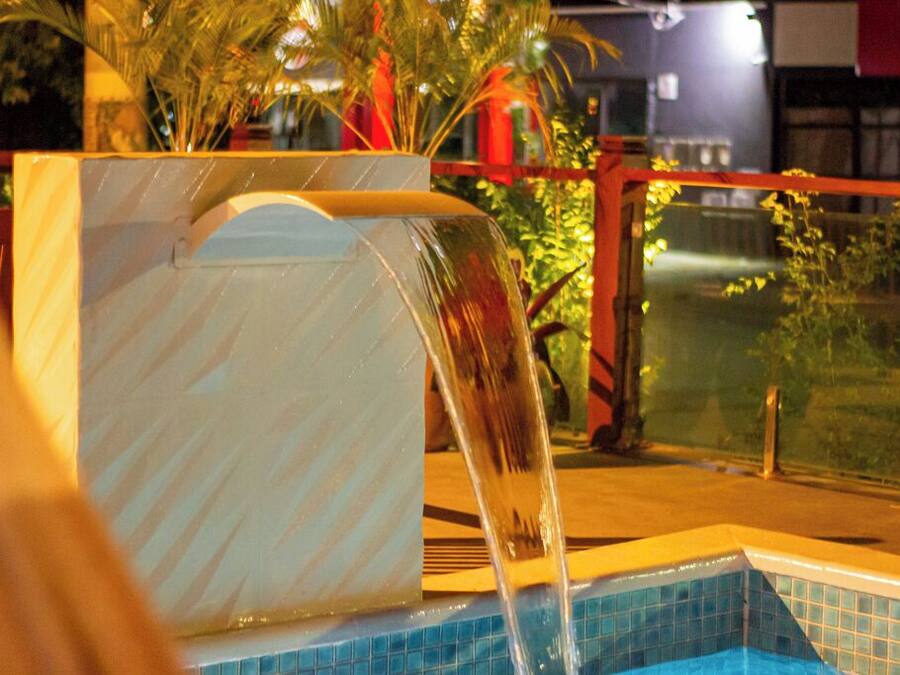 Piscina com um elemento aquático, cercada por um revestimento de vidro e palmeiras.